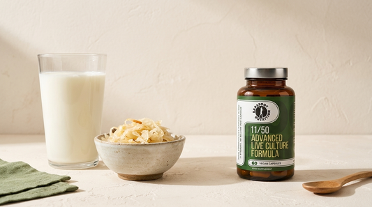 A glass of kefir and a bowl of sauerkraut beside a Barefoot Nutrition Advanced Live Culture Formula bottle on a warm cream tabletop